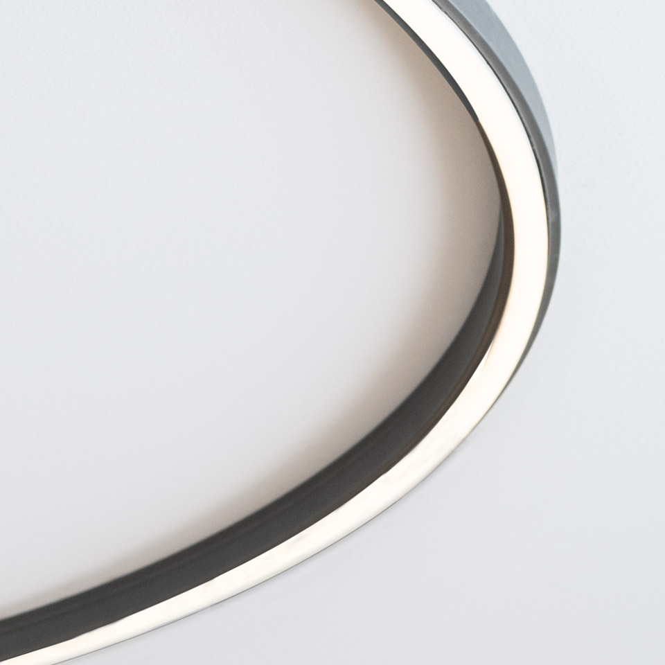 Close-up of Artemide Turn Around System: circular LED ring with dark metal frame emitting warm white light against white background