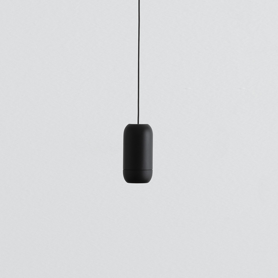 Artemide Turn Around pendant lamp, matte black capsule-shaped body suspended from a black cord against a light grey background