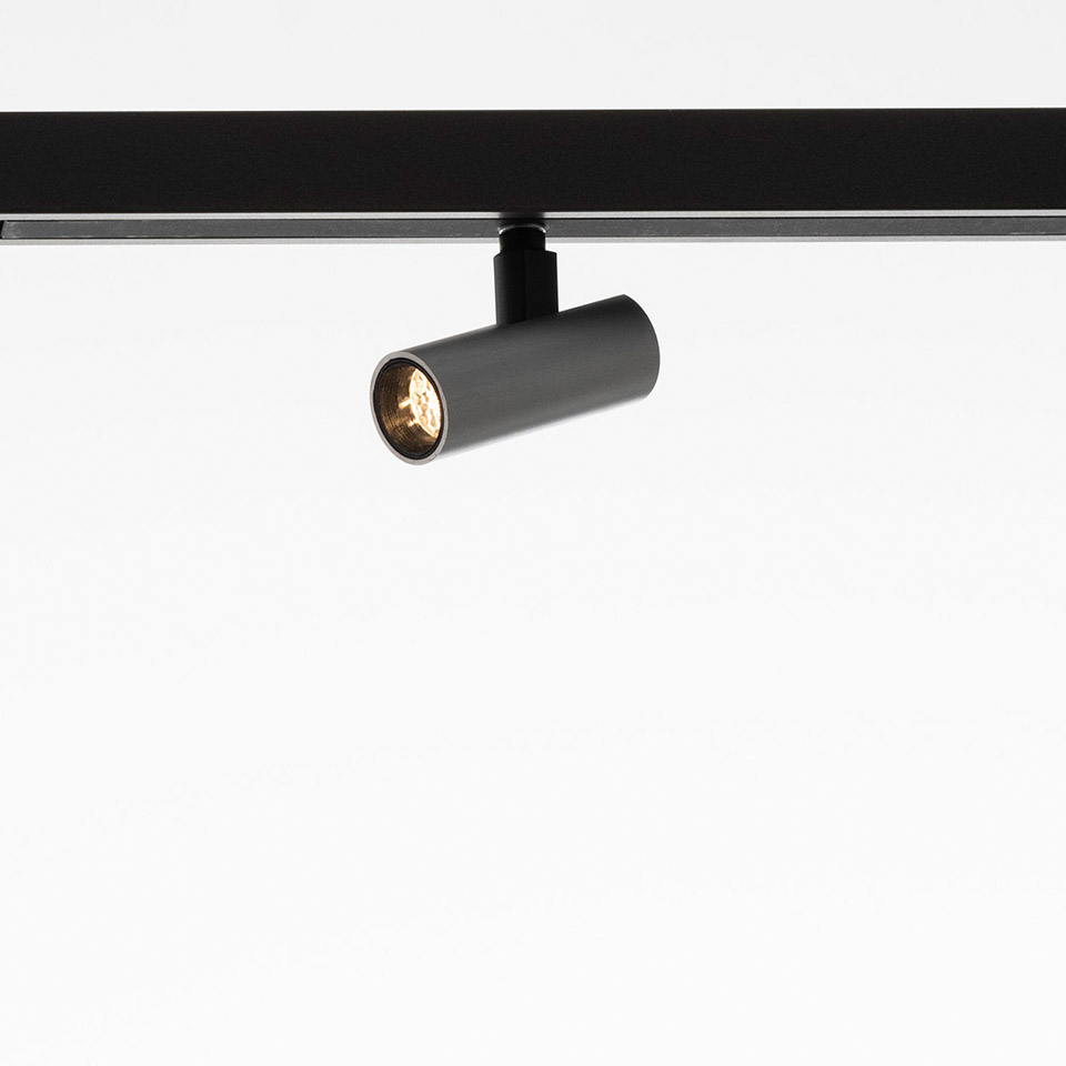 Artemide Turn Around System: adjustable cylindrical grey spotlight mounted on a black track rail, directed downward