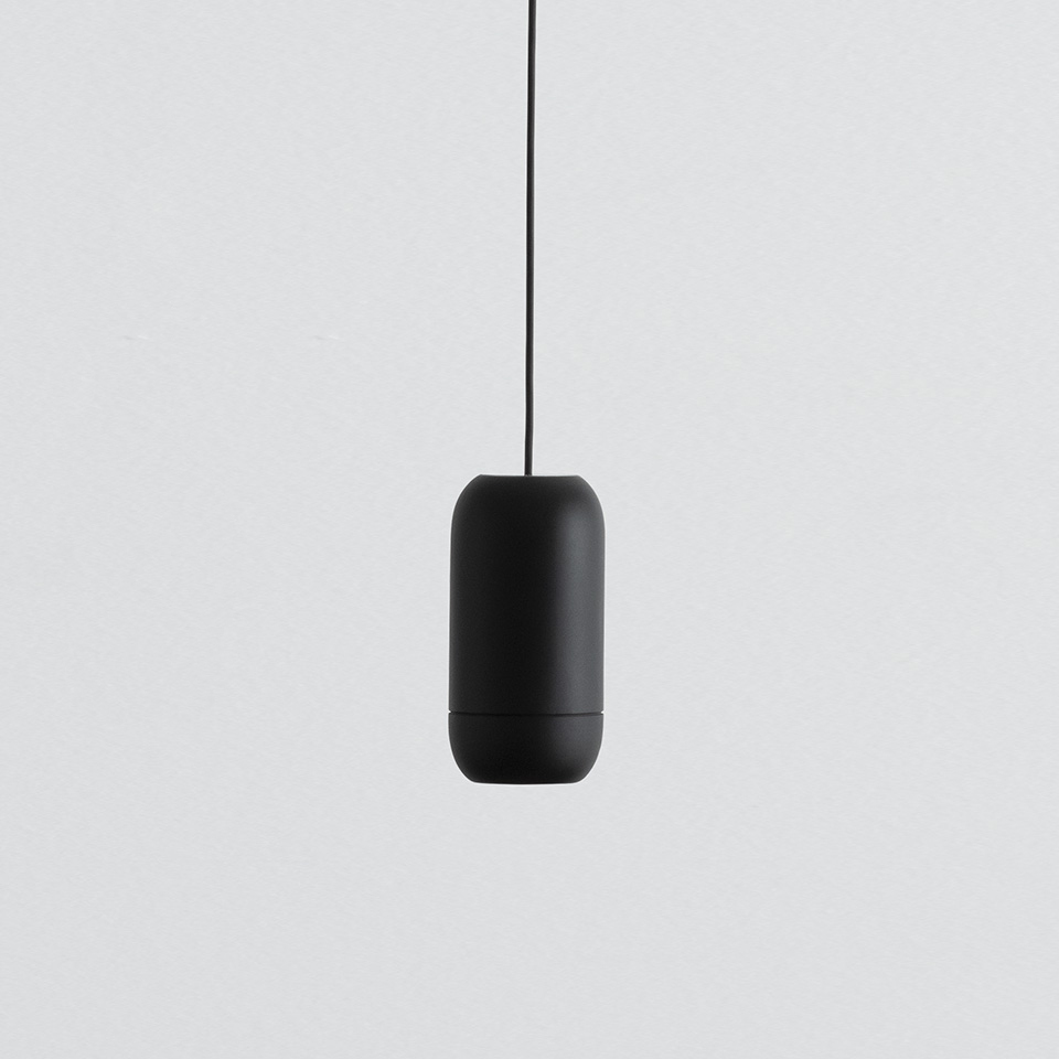 Artemide Turn Around pendant lamp, matte black capsule-shaped body suspended by a black cord against a light grey background