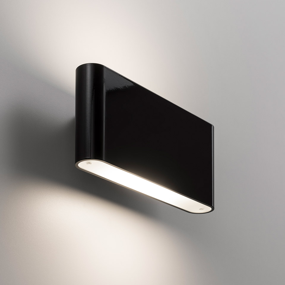 Artemide Two Flags Parete wall lamp in black, rectangular body emitting warm white light from bottom diffuser, casting soft glow on wall
