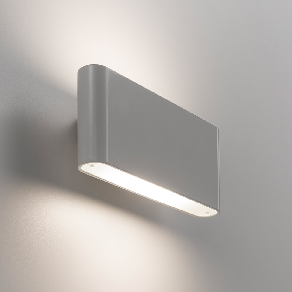 Artemide Two Flags Parete wall lamp in grey, rectangular body emitting warm white light downward, casting soft glow on wall