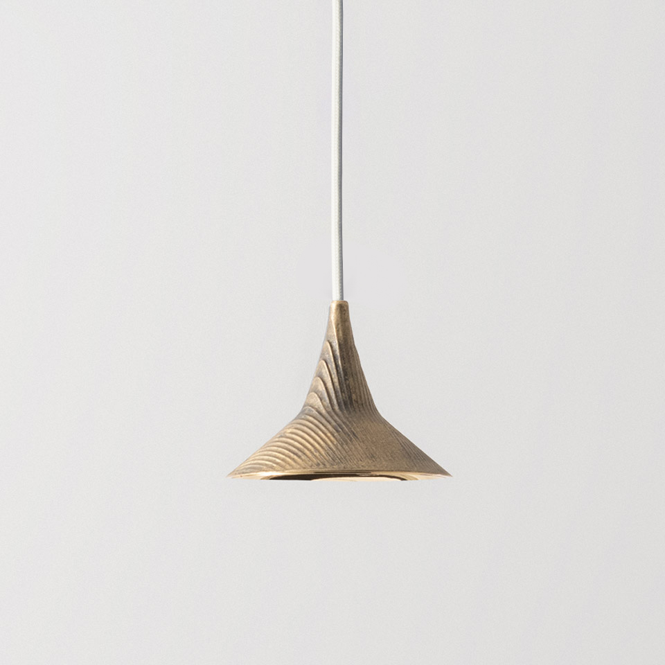 Artemide Unterlinden pendant lamp with flared brass shade featuring concentric ribbed texture, suspended by a thin white cord