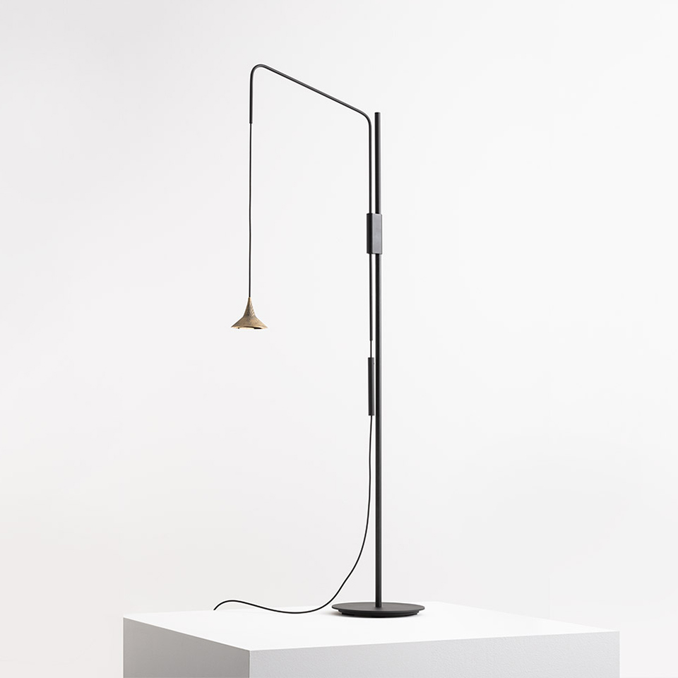 Artemide Unterlinden floor lamp: tall black stem with adjustable arm, small brass conical shade, circular base on white pedestal