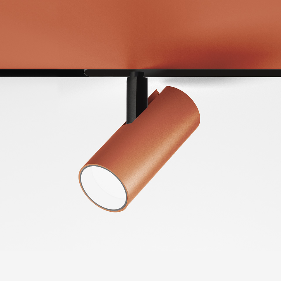 Artemide Vector Magnetic track spotlight in terracotta finish, cylindrical body on black rail mount, tilted downward