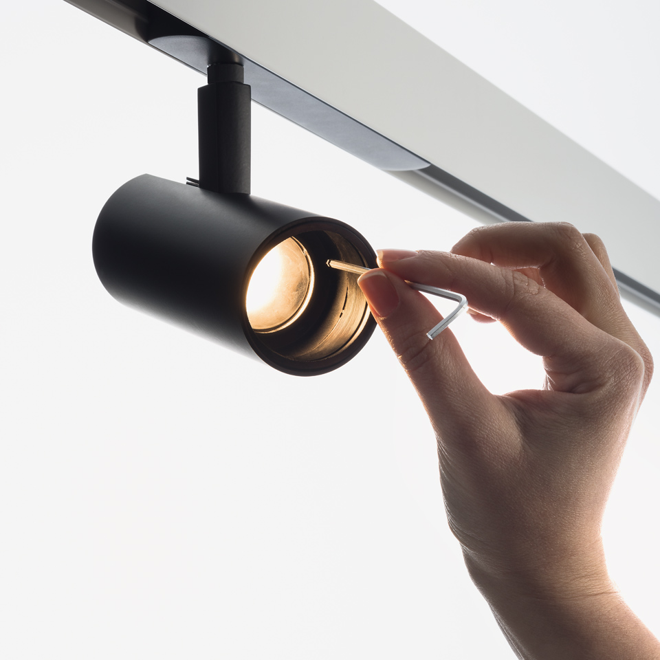 Hand adjusting the lens of an Artemide Vector Track 230V black cylindrical spotlight mounted on a ceiling track system. - 2