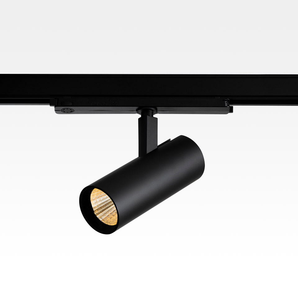 Artemide Vector Track 230V: black cylindrical LED spotlight mounted on a black track rail, tilted downward, warm light visible