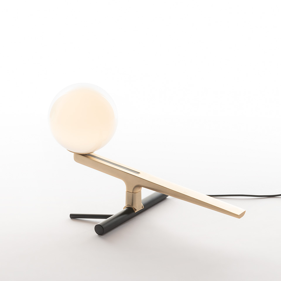 Artemide Yanzi table lamp: angled brass arm with opal glass sphere, resting on a black cylindrical base