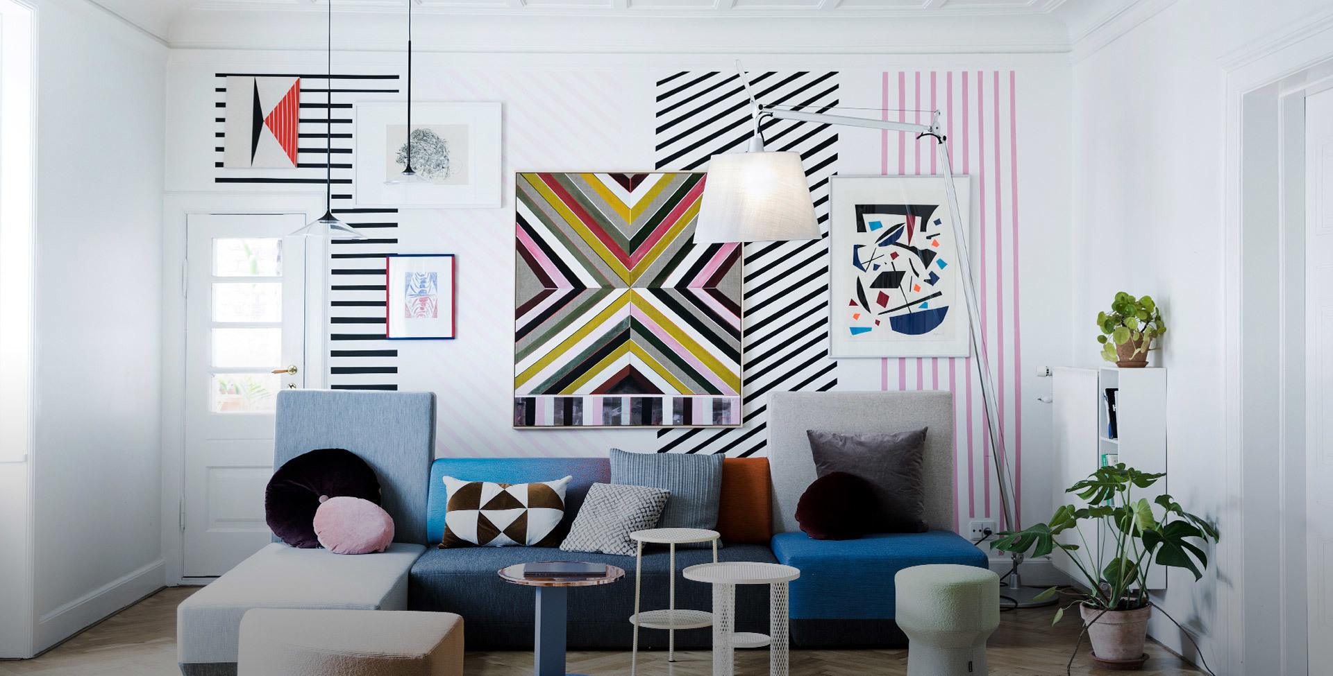 Colorful living room with blue sofa, bold geometric wall art, and two Artemide pendant lamps with white conical shades hanging from ceiling