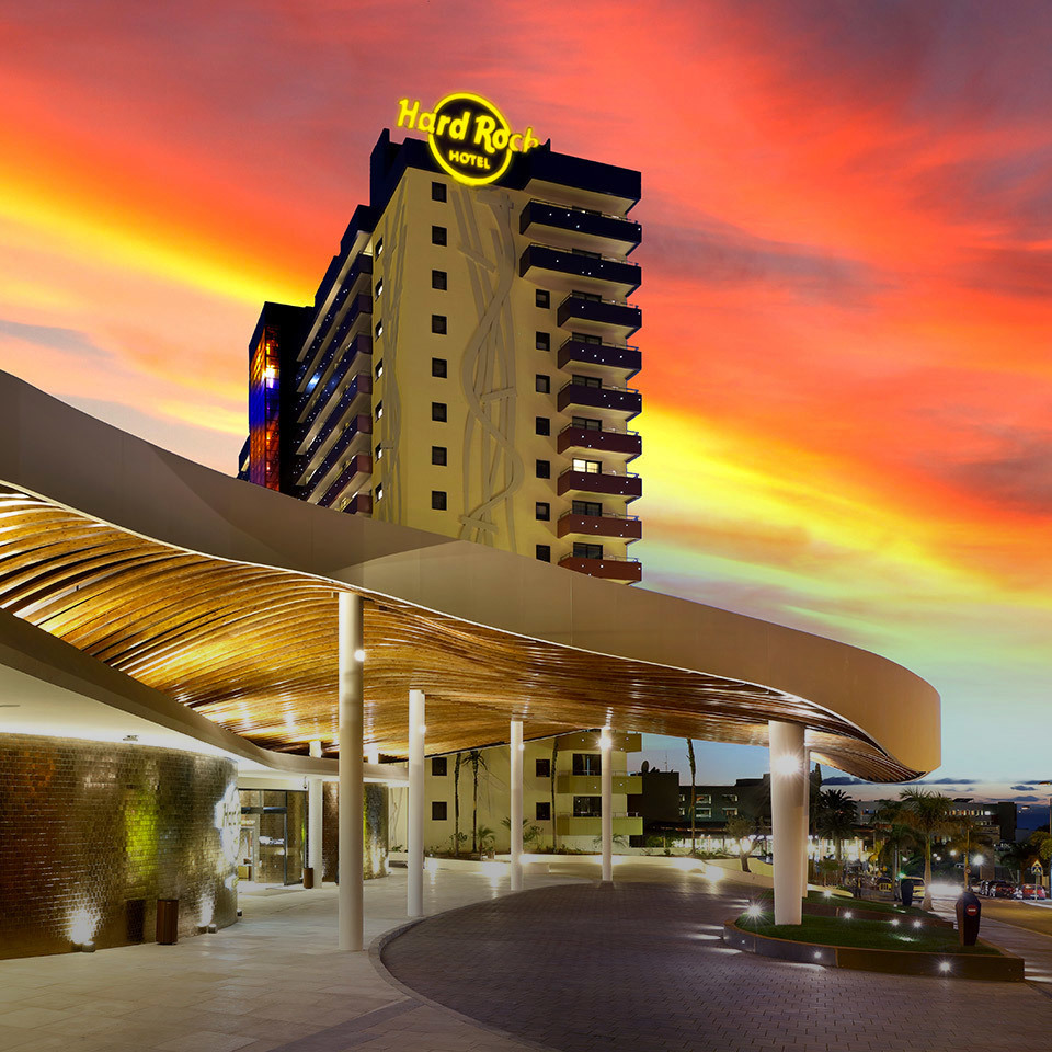 Hard Rock Hotel entrance at dusk, featuring a curved illuminated canopy with warm golden lighting under a dramatic red sky
