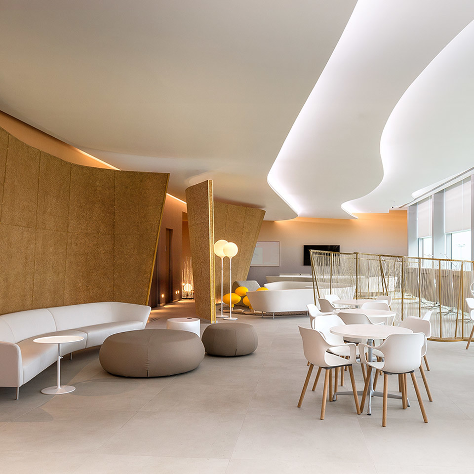 Modern lounge with curved cork walls, white sofas, round ottomans, and Artemide floor lamps with spherical diffusers providing warm ambient light