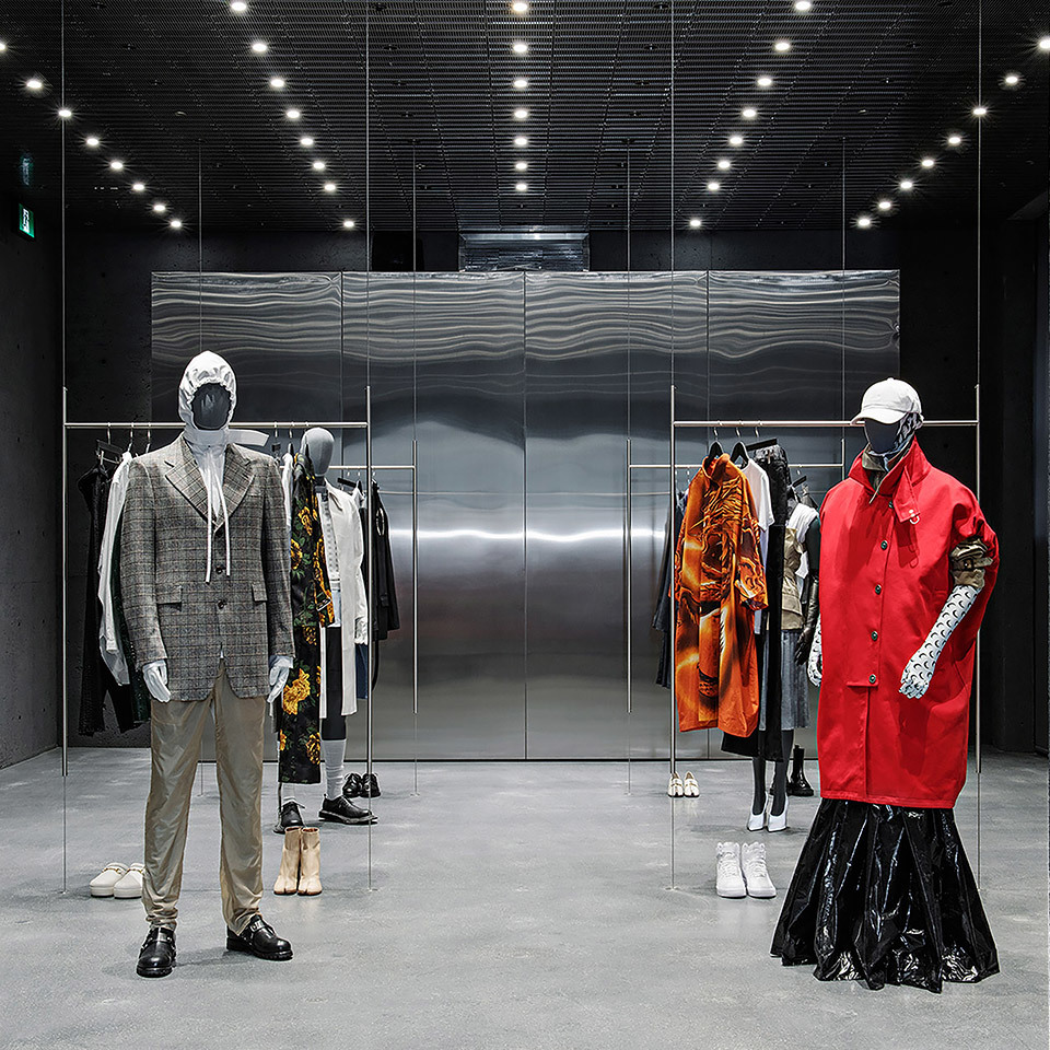 Fashion boutique interior with recessed ceiling spotlights illuminating mannequins in designer outfits, metallic wall backdrop, concrete floor