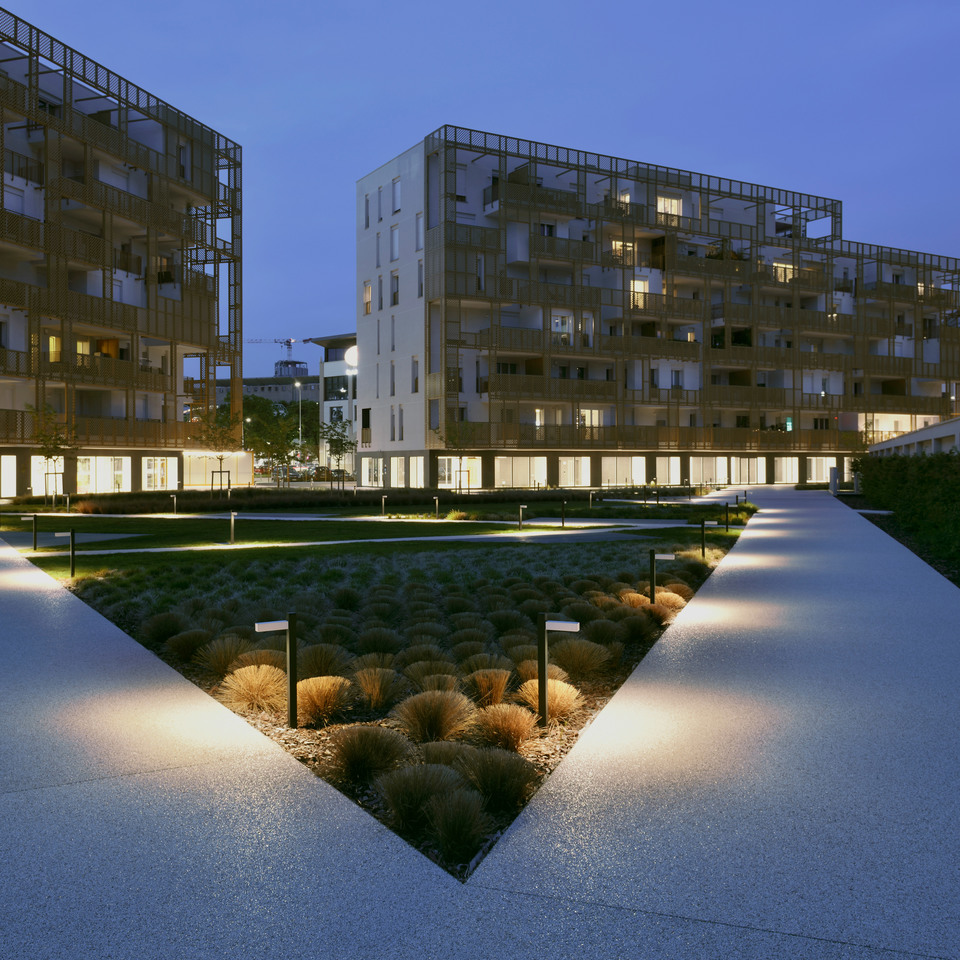 Artemide bollard lights illuminate a landscaped pedestrian path at dusk, flanked by ornamental grasses and modern residential buildings