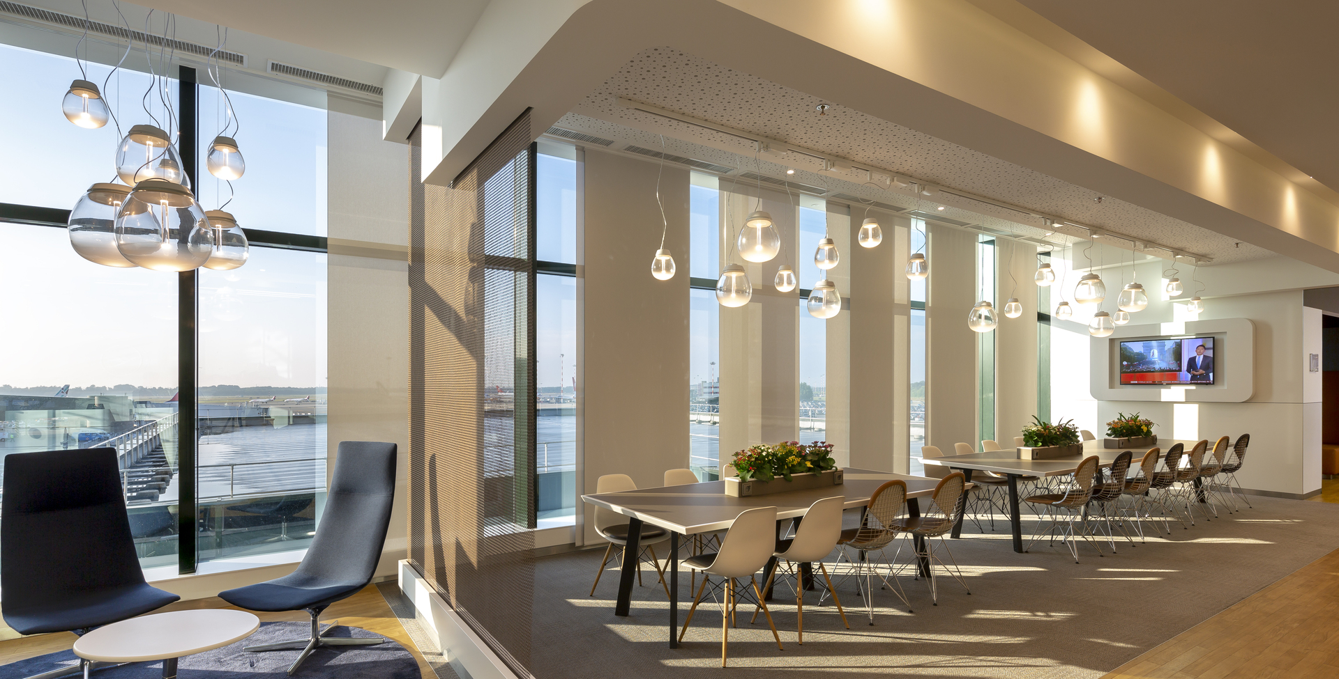 Modern office lounge with Artemide pendant lights: spherical chrome drops over dining area, metallic cluster over seating, floor-to-ceiling windows