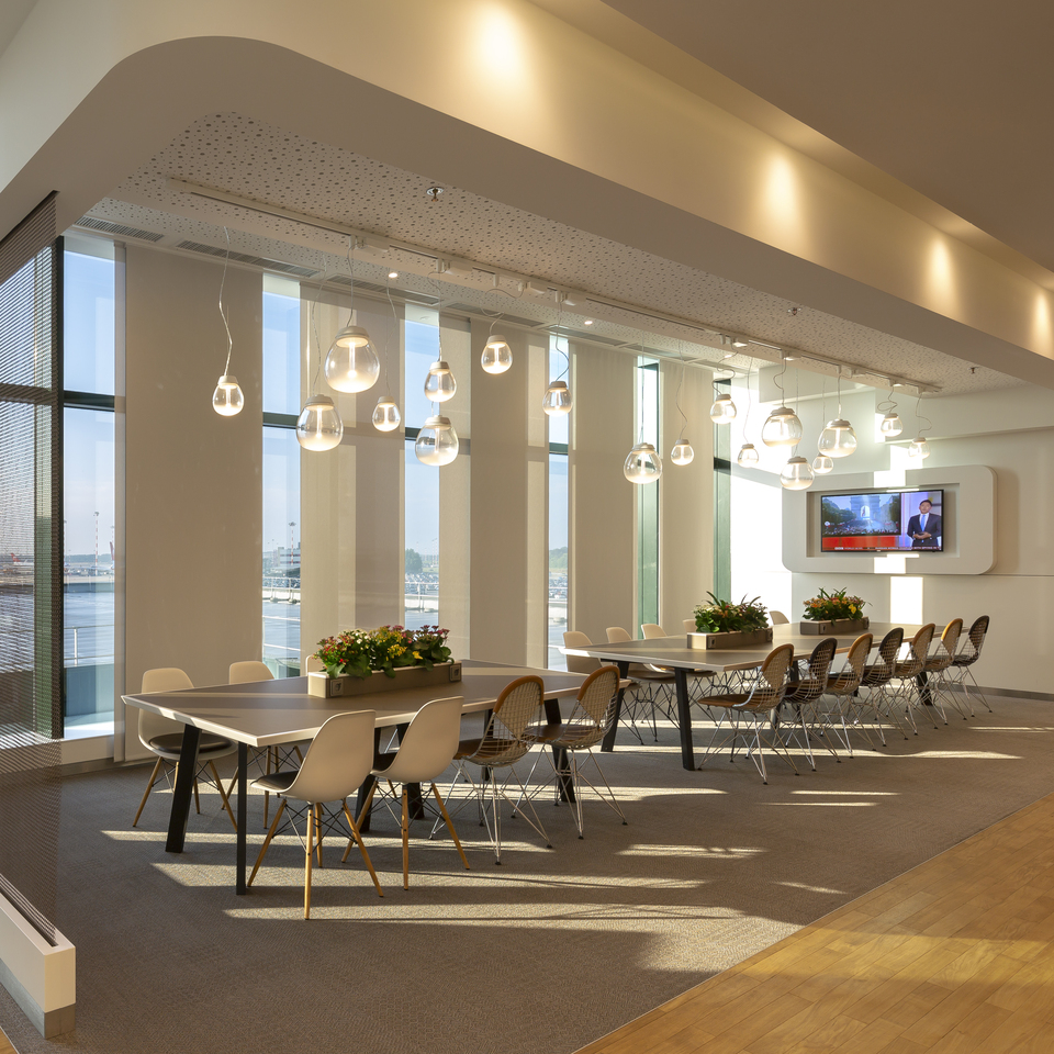 Modern office dining area with Artemide pendant globe lights hanging over long tables with white Eames-style chairs and city views.
