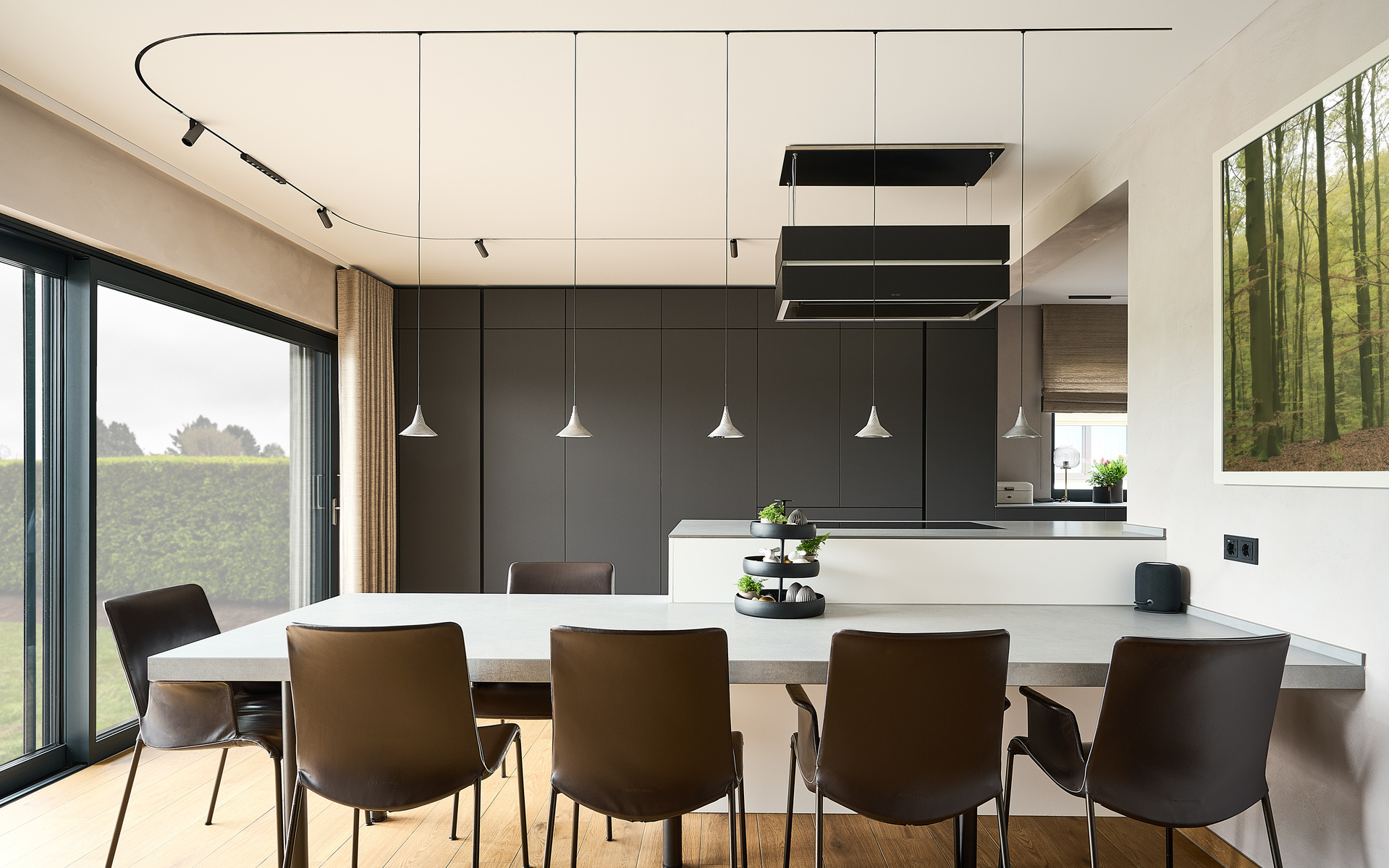 Modern dining room with white table, dark chairs, and three conical white pendant lights hanging above on black cables.
