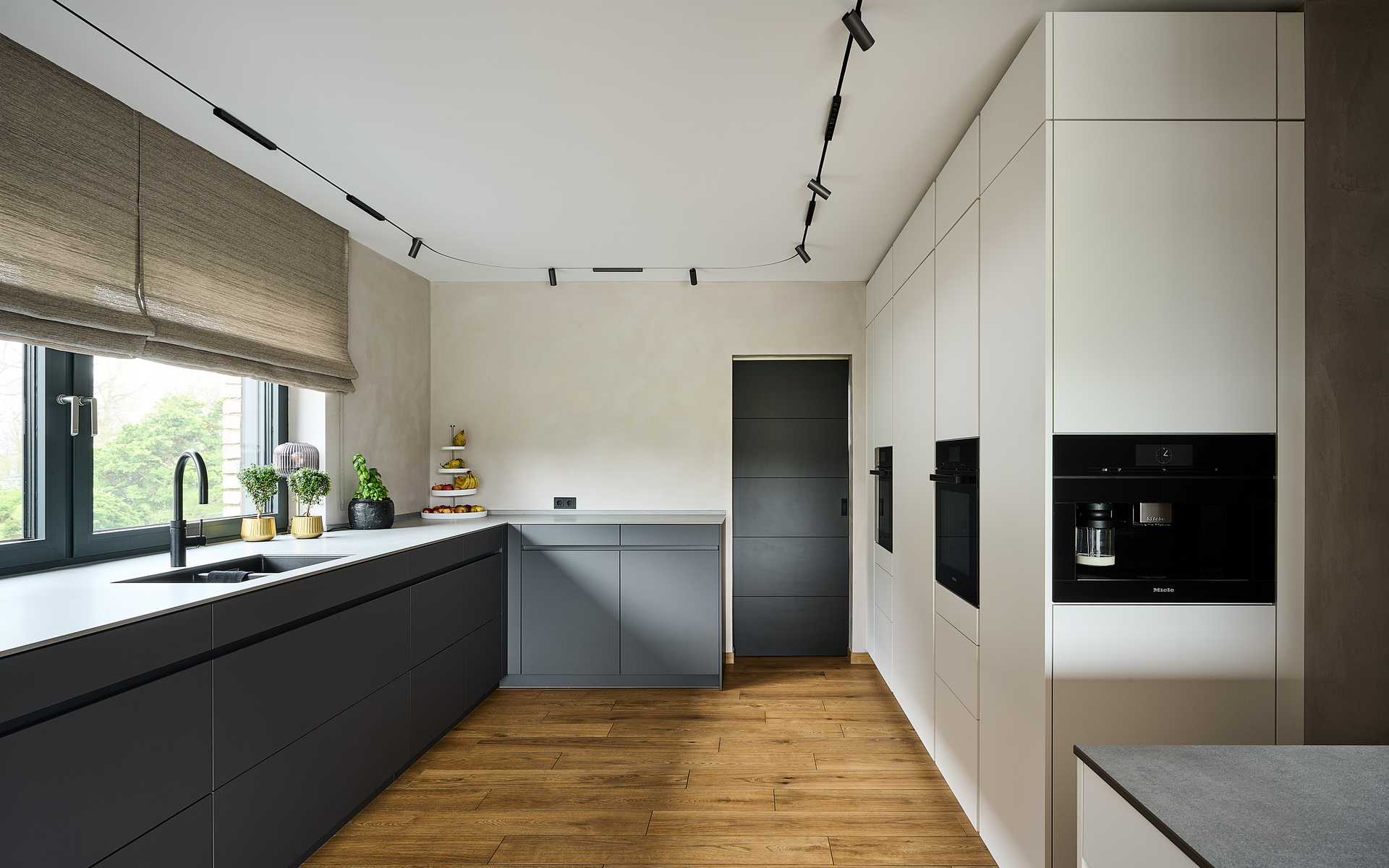 Modern kitchen with dark cabinetry and white units, illuminated by Artemide track spotlights mounted on black ceiling rails