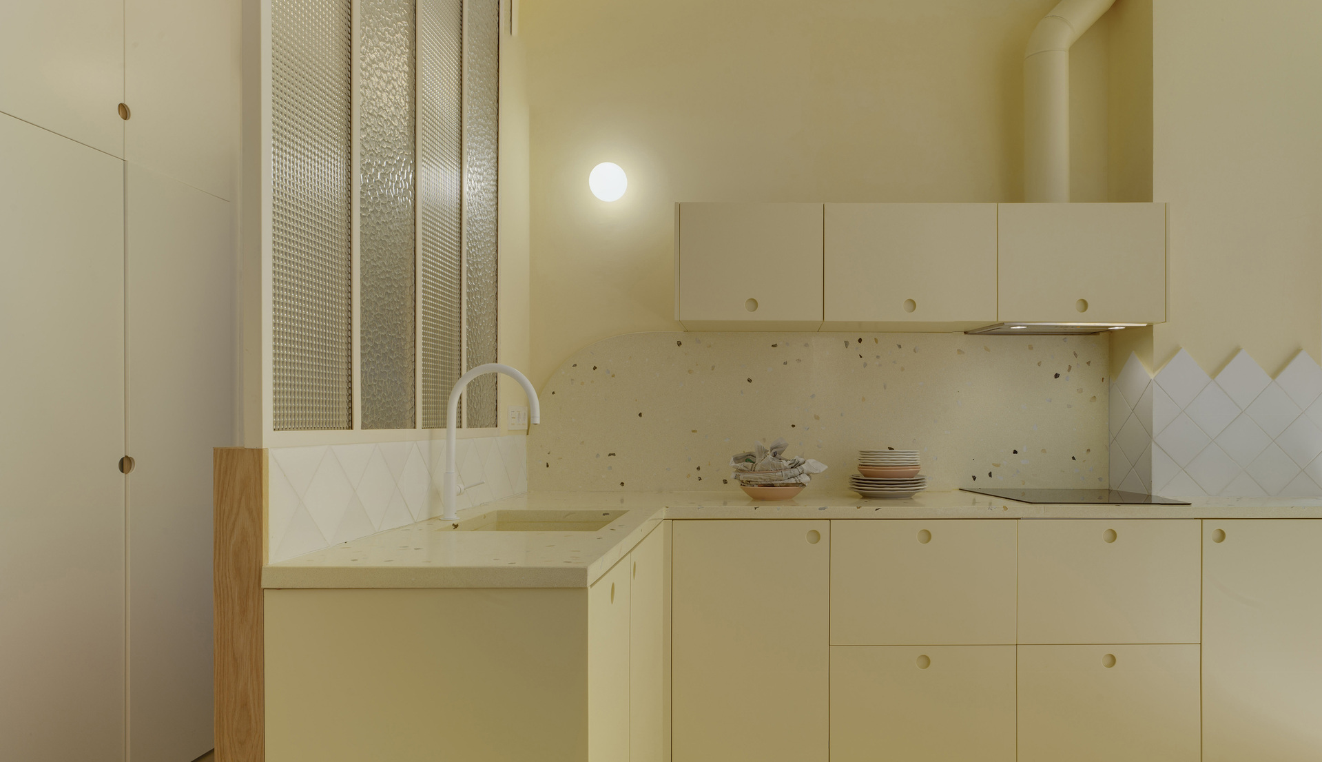 Detail of the kitchen with cream-colored cabinets, textured glass partition, and wall light.
