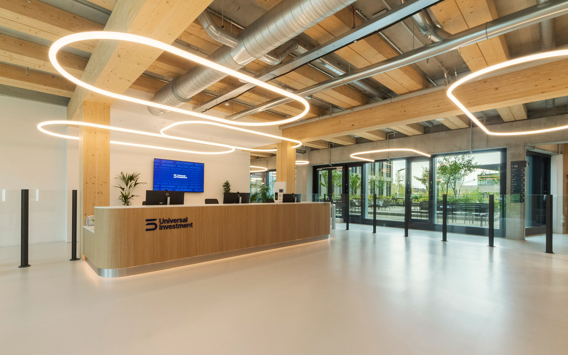 Modern office lobby with oval Artemide pendant lights on wood-beam ceiling, illuminating a reception desk with Universal Investment branding.