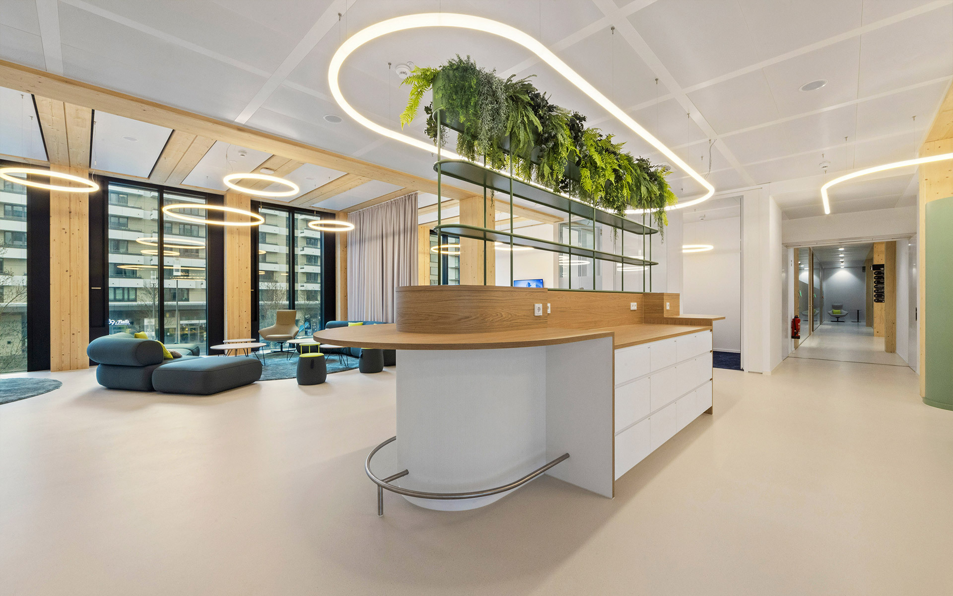 Modern office reception with curved white desk, living green wall, and Artemide circular LED pendant lights illuminating an open workspace.