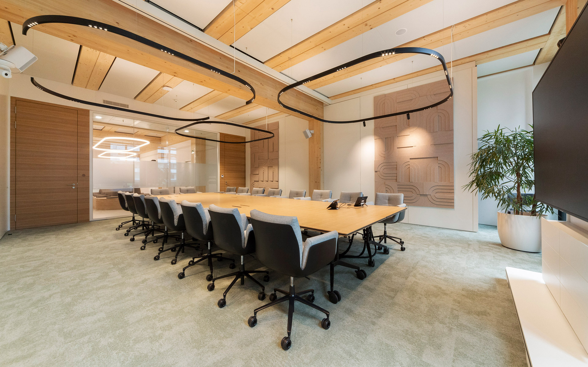 Modern conference room with large wooden table, black chairs, and two oval black Artemide pendant lights suspended from a wood-paneled ceiling.