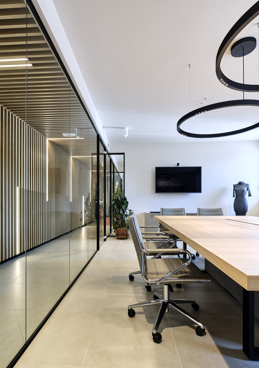 Modern conference room with Artemide circular black pendant lights above a long wooden table with ergonomic chairs and glass partition wall.