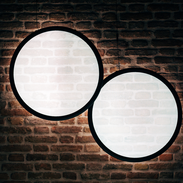 Two large circular pendant lamps with black frames and white diffusers, suspended against a rustic exposed brick wall.