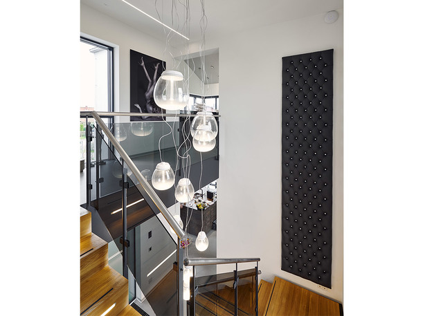 Cluster of Artemide Muse pendant lamps with glass shades hanging over a modern staircase with glass railings and wood steps.
