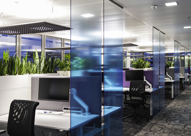Modern open-plan office with glass partitions, workstations, and recessed ceiling LED panels providing bright, uniform lighting.