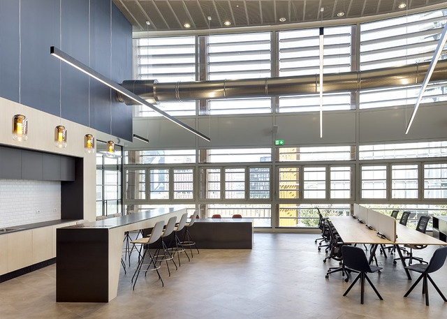 Modern open-plan office with linear pendant lights over a dark kitchen island and small amber glass pendants on the left wall.
