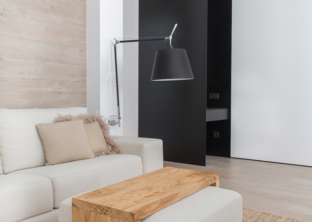 Artemide Tolomeo Mega wall lamp with black shade on adjustable arm, illuminating a modern living room with white sofa and wood coffee table