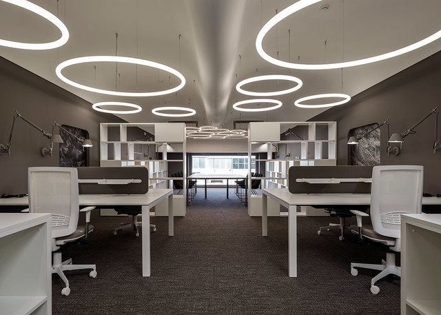 Modern office with rows of white desks and Artemide circular ring pendant lights arranged on the ceiling, creating bright ambient lighting.