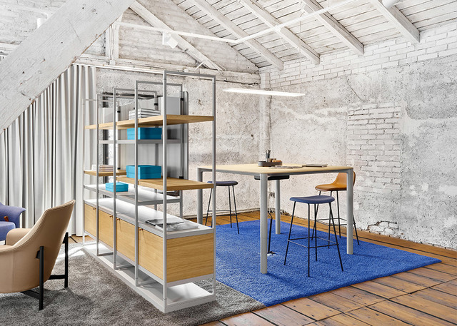 Modern workspace with Artemide linear pendant light over a standing desk, modular shelving unit, blue rug, and exposed brick walls