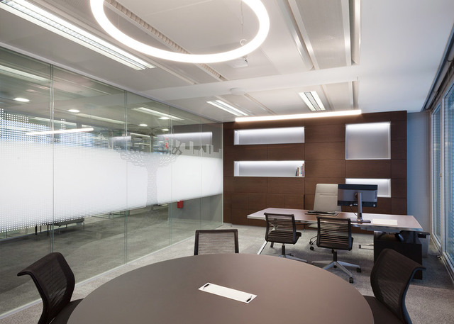 Modern office with Artemide circular LED ring pendant light on ceiling, illuminating a meeting table and executive desk area.