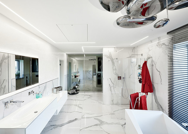 Luxurious marble bathroom with recessed linear LED lighting on ceiling and chrome pendant lamps above a freestanding bathtub