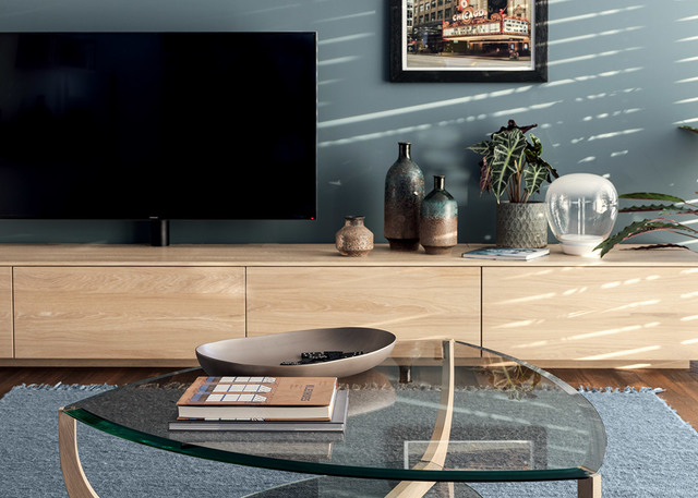 Modern living room with glass coffee table, light wood TV unit, decorative vases, and a spherical glass table lamp on the sideboard