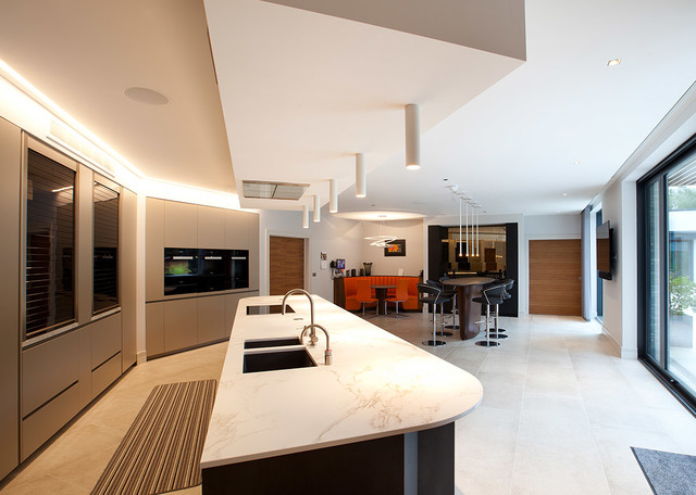 Modern open-plan kitchen with marble island, recessed ceiling lights, and pendant lamps illuminating a dining and lounge area beyond.