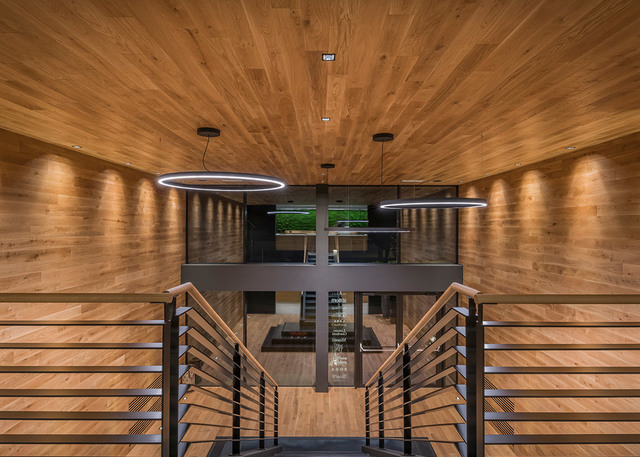 Two circular LED pendant lights hang over a wood-paneled staircase and mezzanine, with recessed and wall-mounted spotlights.