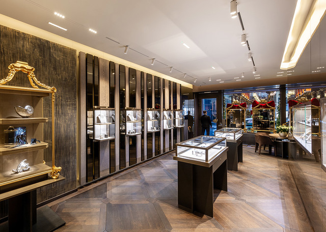 Luxury jewelry boutique interior with Artemide track lighting illuminating display cases and wall-mounted showcases on herringbone wood floor