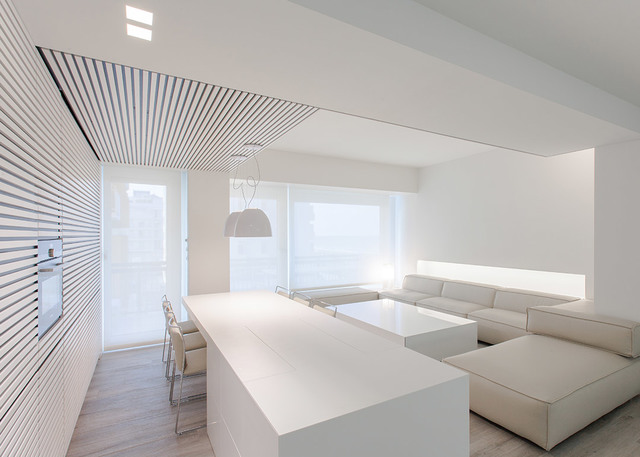 Minimalist all-white open living space with a large pendant lamp, recessed ceiling lights, kitchen island, and L-shaped sofa.