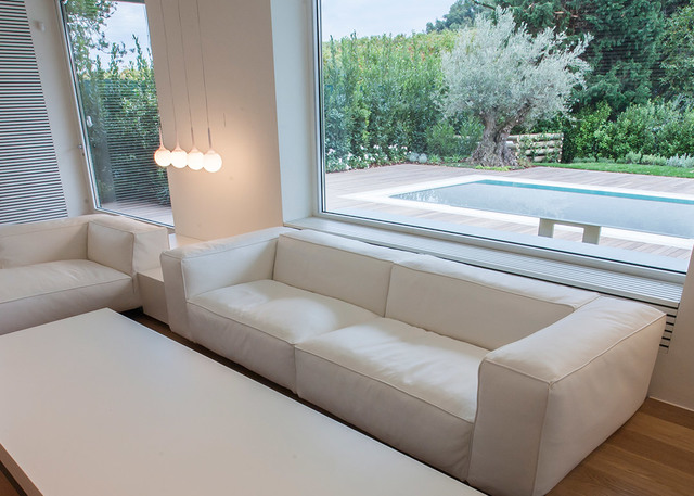 Modern living room with white sofas and Artemide pendant lights with spherical globes, overlooking a garden with pool.