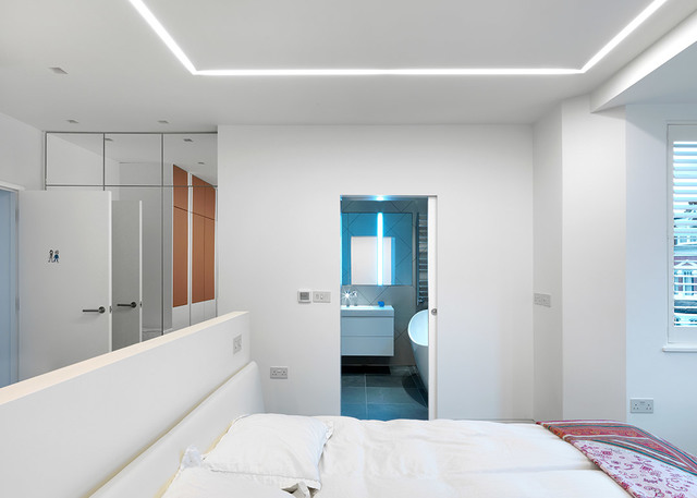 Modern white bedroom with recessed LED cove lighting along ceiling perimeter, illuminating the room softly above a double bed.
