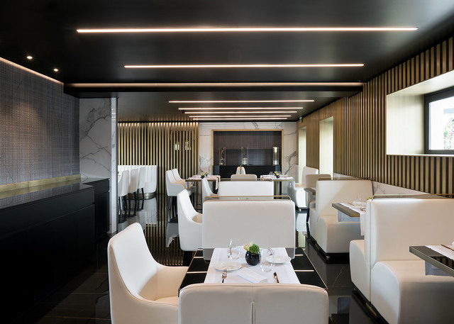 Elegant restaurant interior with recessed linear LED ceiling lights illuminating white chairs, booths, and marble accents on black floor.
