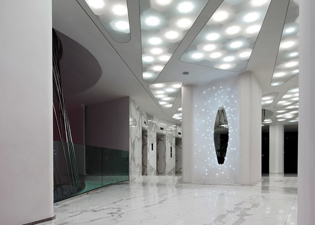 Modern lobby with circular recessed LED ceiling lights illuminating a marble floor and a glowing oval decorative wall panel.