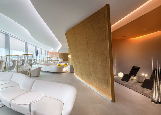 Modern lounge with white curved sofas, warm cove lighting on ceiling, golden partition wall, and floor lamps in a relaxation area
