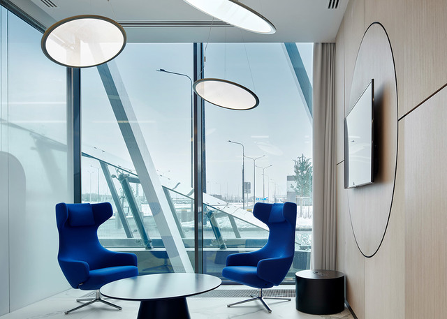 Modern lounge with two Artemide Alphabet of Light circular pendants above blue armchairs, floor-to-ceiling windows, and a decorative wall circle.