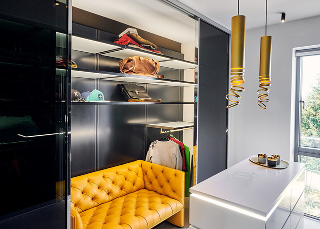 Boutique dressing room with gold spiral pendant lamps, yellow tufted sofa, dark shelving with accessories, and a white counter.