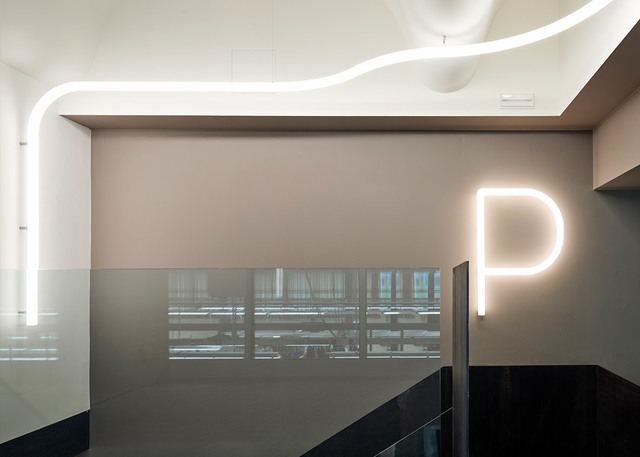 Interior space with sinuous white LED strip light on ceiling and illuminated letter P sign on beige wall above glass partition