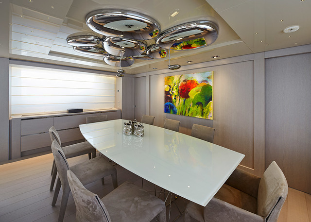 Modern dining room with a sculptural chrome bubble ceiling light above a white glass table surrounded by grey upholstered chairs