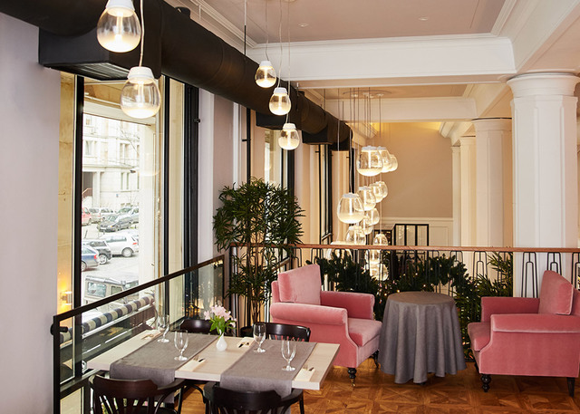 Restaurant interior with Artemide pendant lights hanging over dining tables and pink velvet armchairs near large windows.